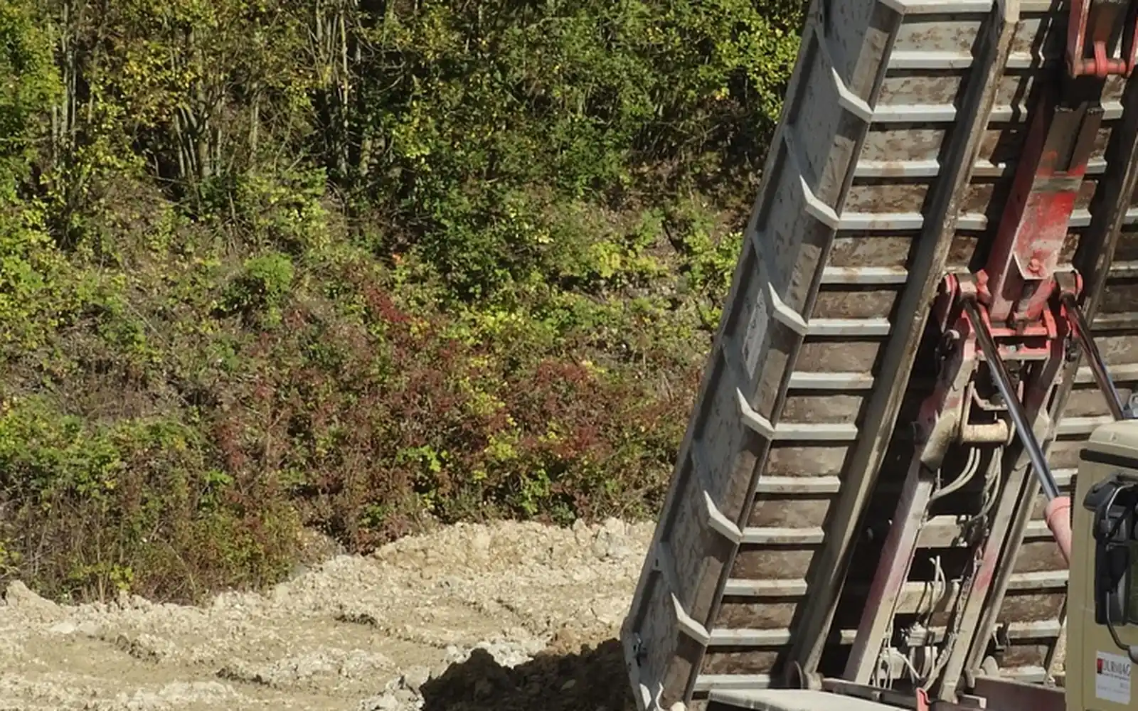 Camion benne qui déverse du gravier devant une entrée